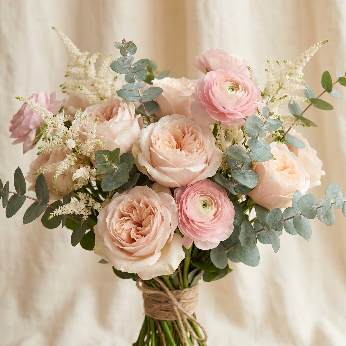 Boeket van zachtroze rozen, ranonkels en eucalyptus, gebonden met touw